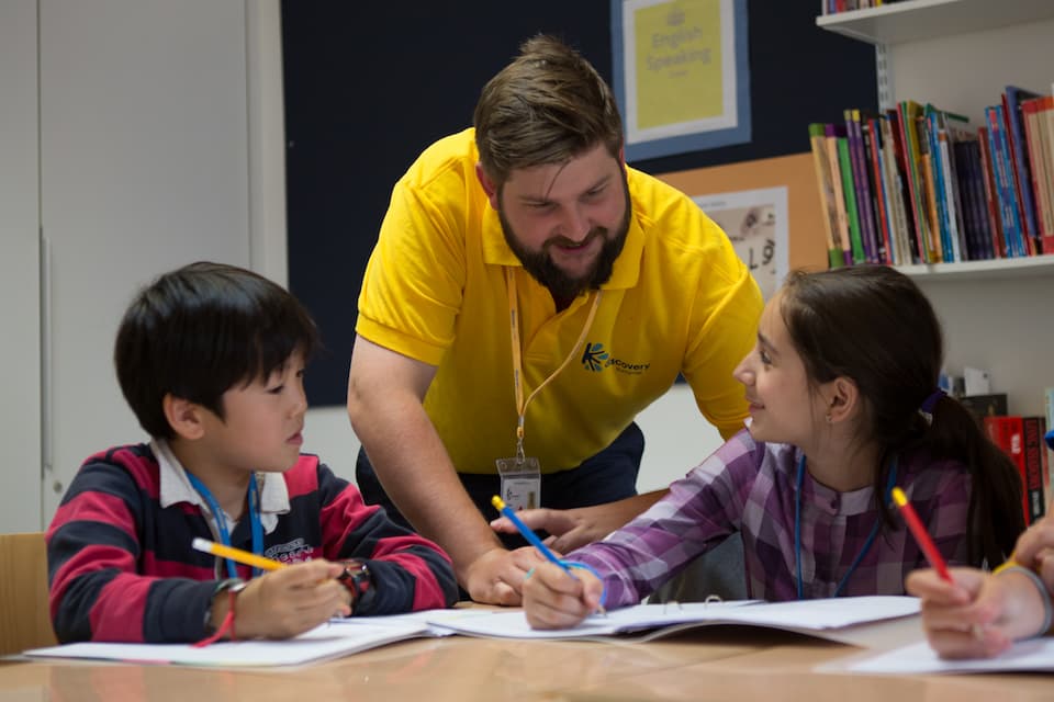 Profesor ayudando a dos alumnos en clase de inglés